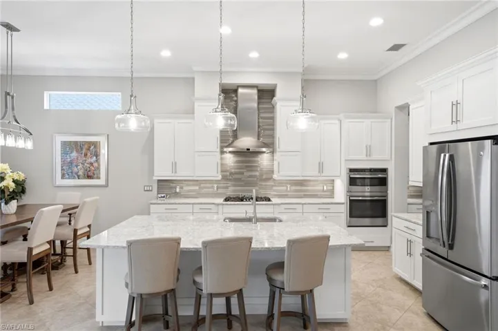 Gourmet kitchen with white wood cabinetry, custom lighting, center island, stainless steel appliances including gas cooking and double oven.