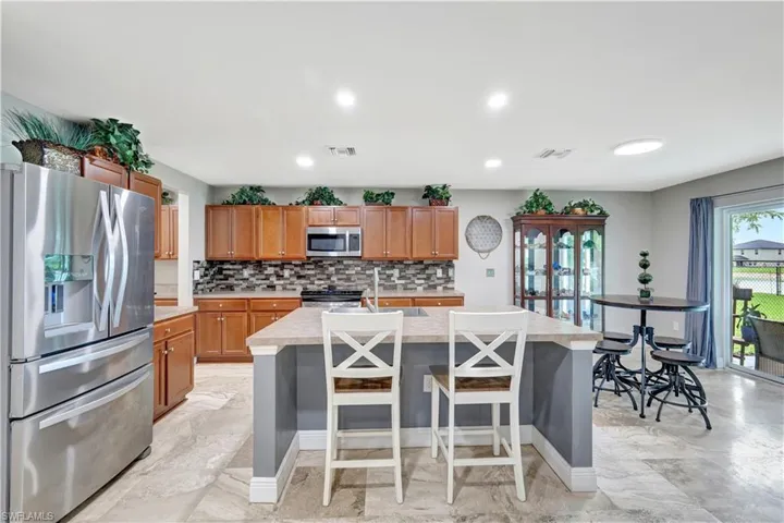 Kitchen with appliances with stainless steel finishes, light countertops, tasteful backsplash, a kitchen bar, and brown cabinets