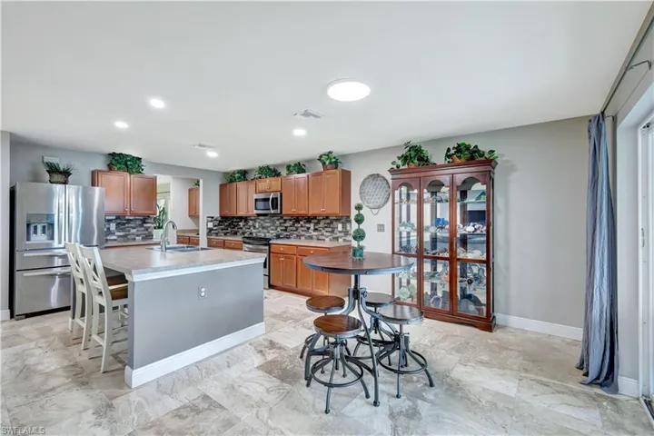 Kitchen featuring appliances with stainless steel finishes, light countertops, tasteful backsplash, brown cabinets, and an island with sink