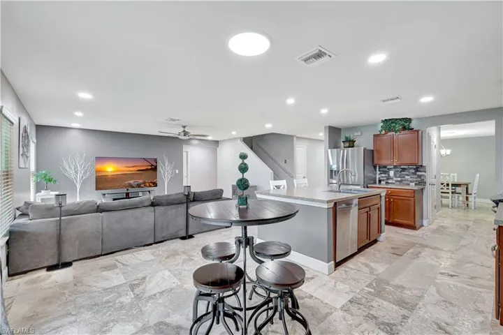 Kitchen with a center island with sink, appliances with stainless steel finishes, ceiling fan, open floor plan, and brown cabinetry