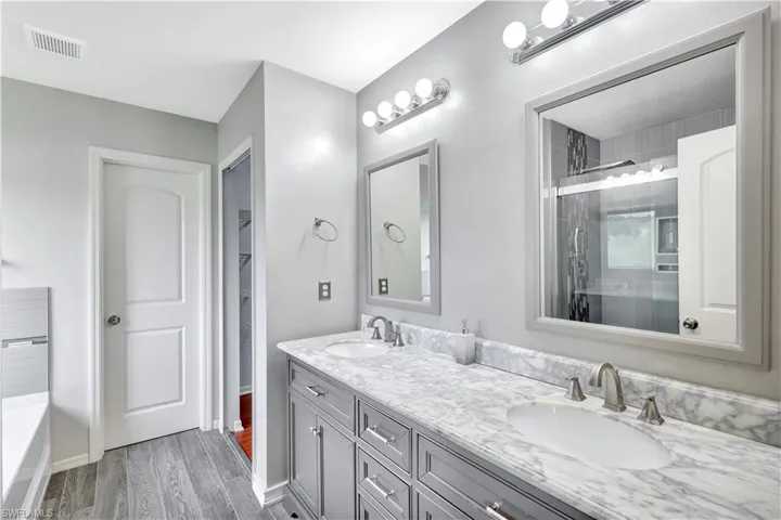 Bathroom featuring a shower stall, double vanity, dark wood-type flooring, a walk in closet, and a bath