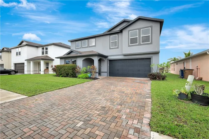 Traditional-style home with stucco siding, a front yard, an attached garage, and decorative driveway