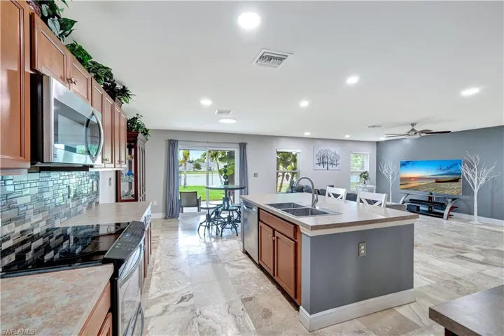 Kitchen featuring stainless steel appliances, brown cabinets, recessed lighting, an island with sink, and backsplash