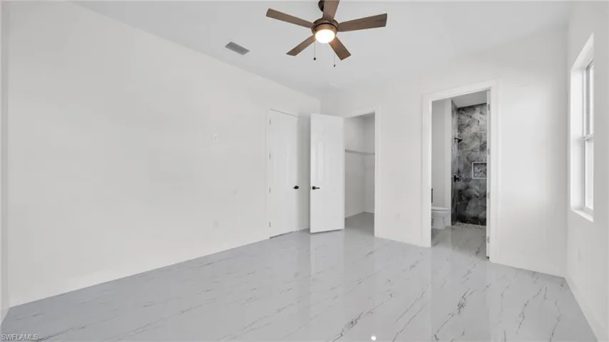 Unfurnished bedroom with light marble finish flooring, a walk in closet, ceiling fan, and connected bathroom
