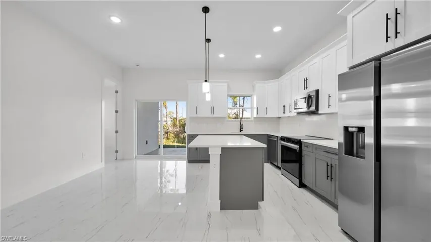 Kitchen with stainless steel appliances, two tone cabinetry, decorative backsplash, a kitchen island, and pendant lighting