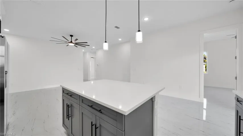 Kitchen with gray cabinets, hanging light fixtures, a kitchen island, light stone countertops, and open floor plan