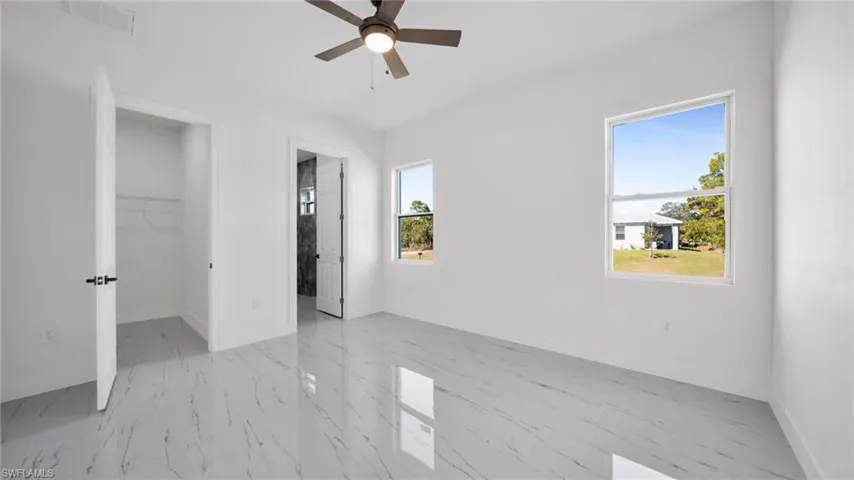 Unfurnished bedroom featuring a spacious closet, ensuite bathroom, a ceiling fan, and light marble finish flooring