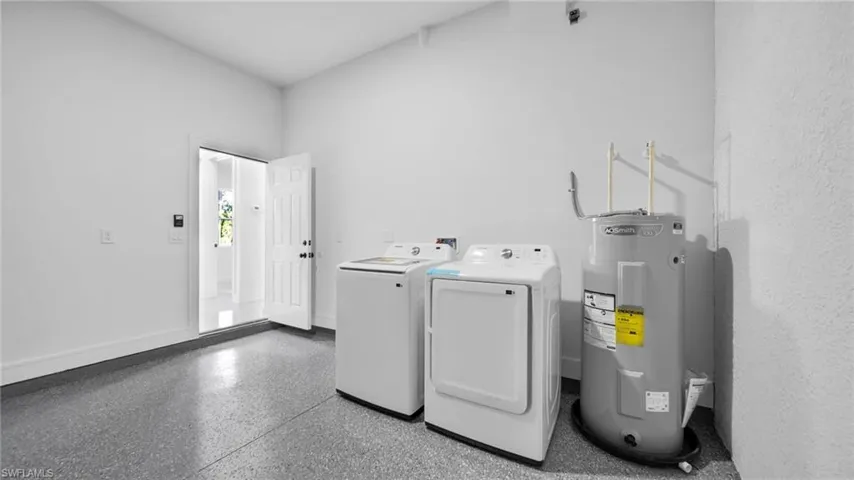 Laundry area with water heater, dark aggregate flooring, and washing machine and clothes dryer