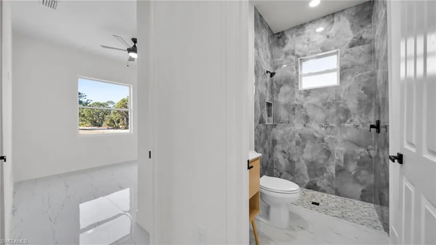 Full bath featuring marble finish flooring, a marble finish shower, vanity, and a ceiling fan