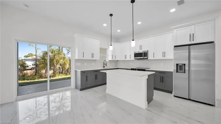 Dual tone kitchen with dual tone cabinets, stainless steel appliances, decorative light fixtures, a kitchen island, and backsplash