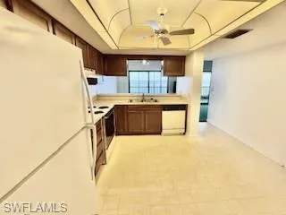 Kitchen with white appliances, a raised ceiling, a ceiling fan, light countertops, and light floors