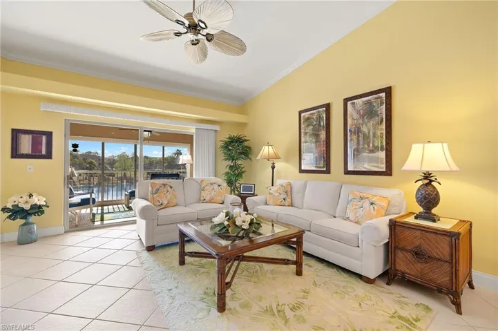 Living area with light neutral tile floors, crown molding, ceiling fan, baseboards, and lofted ceiling