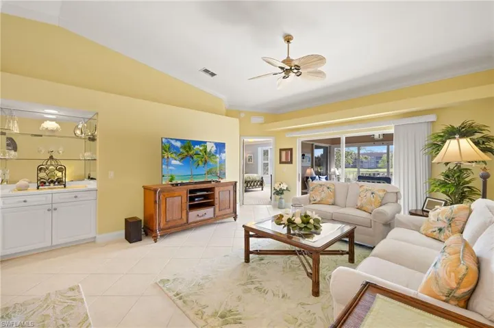 Living area featuring lofted ceiling, baseboards, light tile patterned flooring, ornamental molding, and a ceiling fan