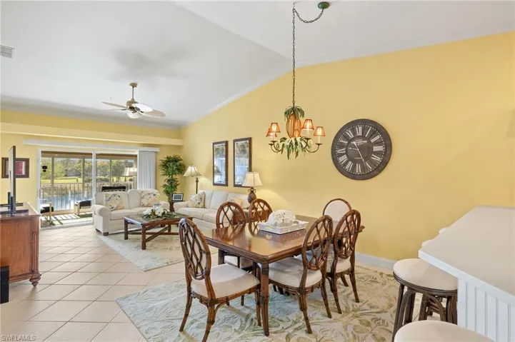 Dining room featuring lofted ceiling, light tile patterned floors, crown molding, visible vents, and ceiling fan with notable chandelier
