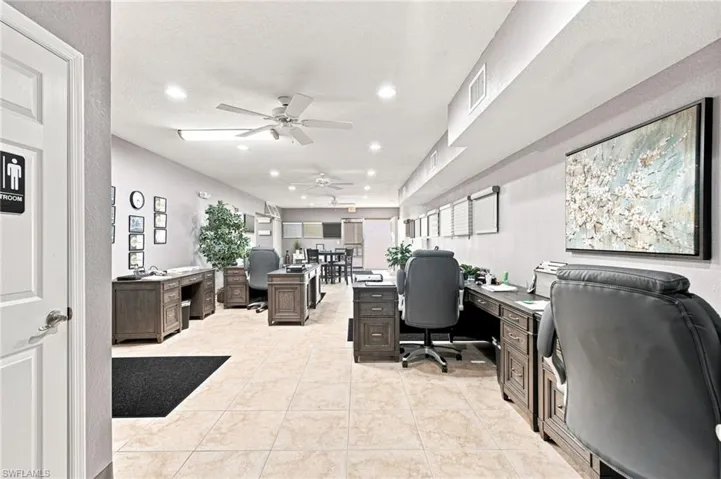 Expansive open-concept workspace featuring recessed lighting, ceiling fans, light-toned tile flooring, and multiple built-in workstations