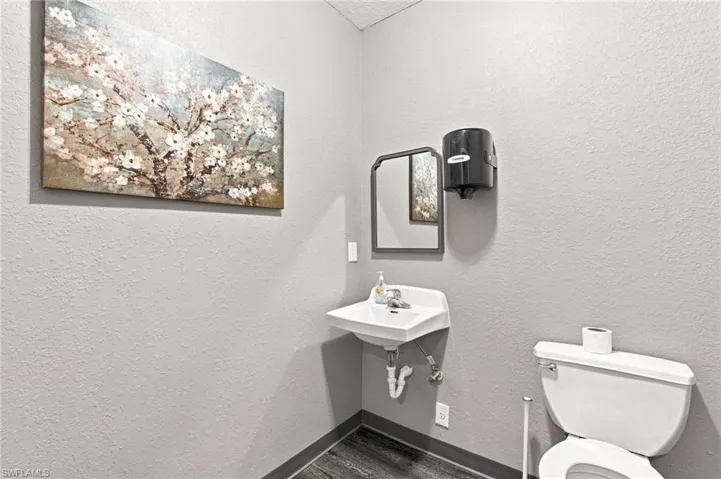 Wall-mounted sink with chrome faucet, toilet, and wood-finish flooring
