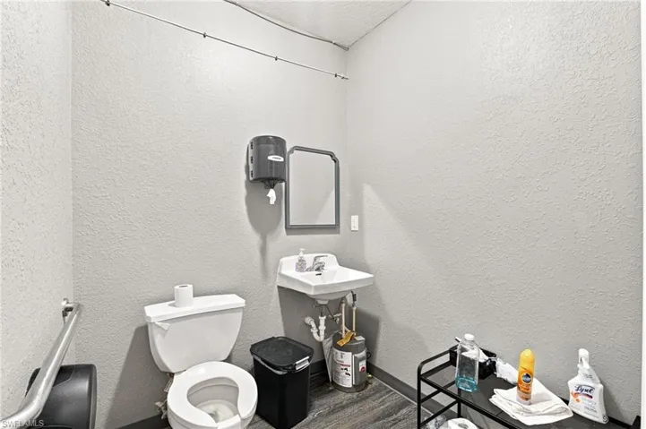 White wall-mounted sink, ceramic toilet, and dark wood-finish flooring