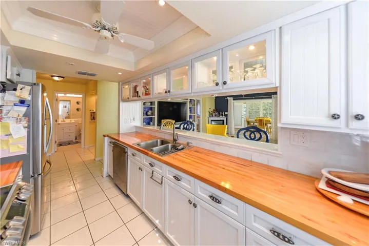 Modern kitchen featuring a stainless steel range with a flat cooktop, white shaker-style cabinetry, butcher block countertops, a tile backsplash, and upper cabinets with glass-paneled doors