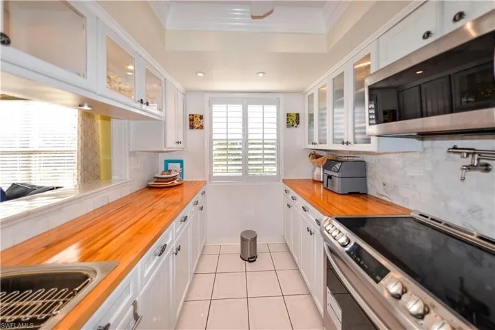 Kitchen featuring wood-finish countertops, stainless steel appliances, white cabinetry, a dual-basin sink with a gooseneck faucet, and shuttered window coverings