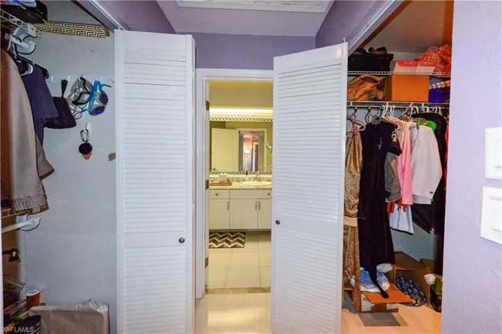 Bathroom featuring a dual vanity with undermount sinks and a light-toned countertop, a large mirror with decorative tile trim, white cabinetry, a glass-enclosed shower with a built-in bench, and tiled flooring