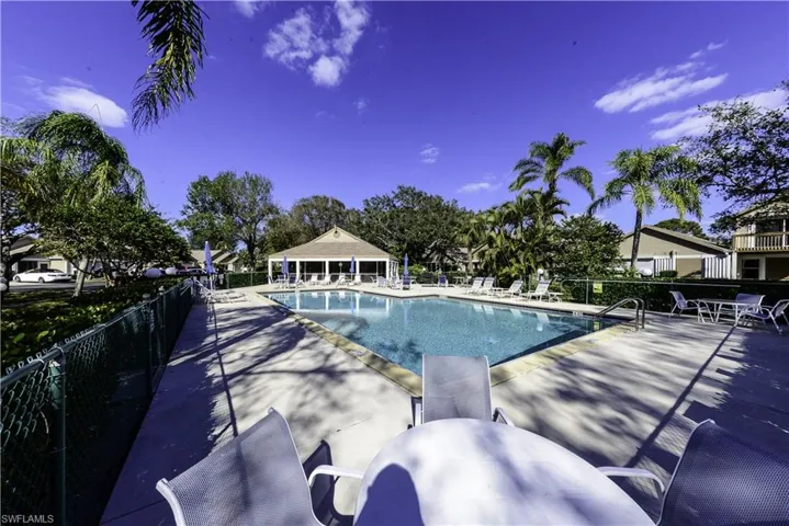 Exterior featuring a paver patio, mature palm trees, a spacious lawn, and a low stone retaining wall