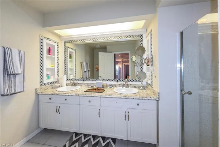 Walk-in shower featuring white tile walls, a built-in corner bench, square mosaic floor tiles, a recessed ceiling light, and a handheld shower fixture