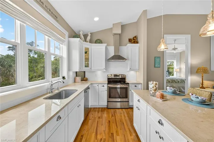 Kitchen featuring stainless steel appliances, lofted ceiling, range hood, light wood floors and white cabinetry