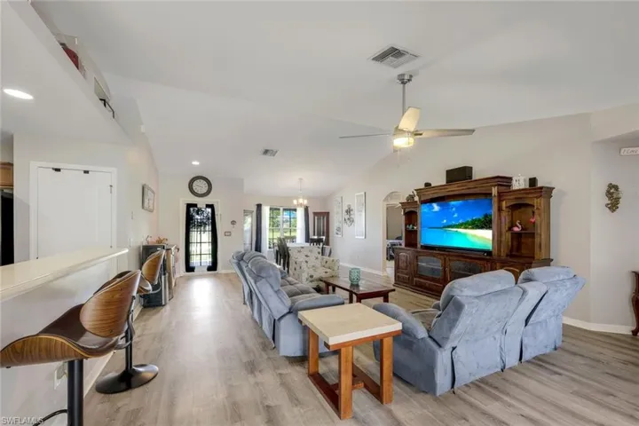 Living room with ceiling fan with notable chandelier, lofted ceiling, and light hardwood / wood-style floors