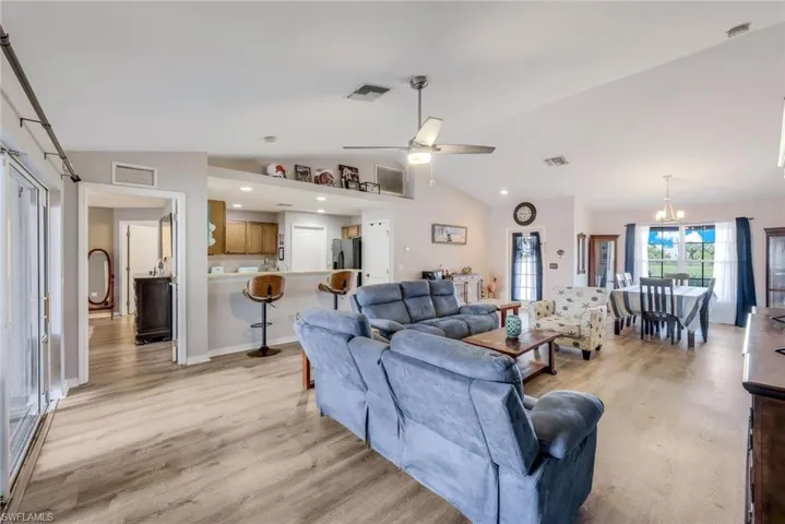 Living room featuring lofted ceiling, ceiling fan with notable chandelier, and light wood-type flooring