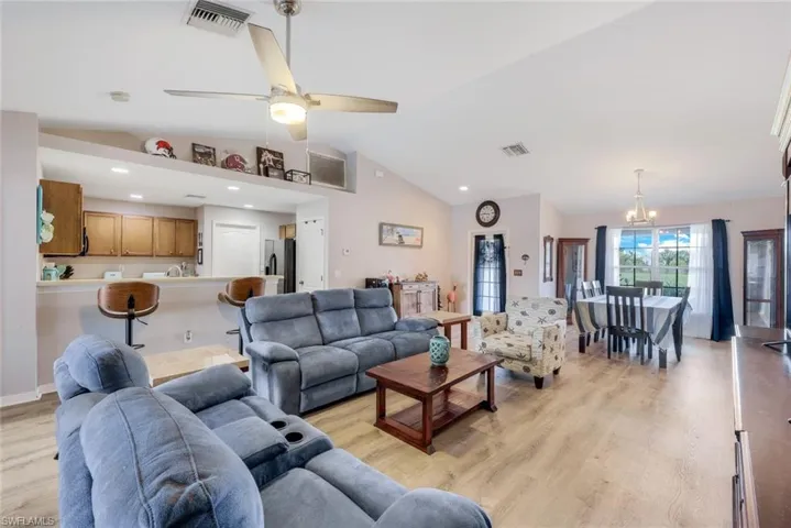 Living room featuring lofted ceiling, ceiling fan with notable chandelier, and light hardwood / wood-style flooring