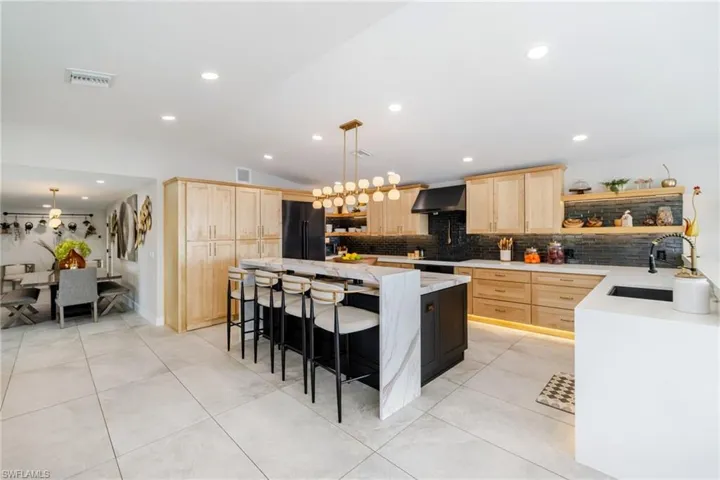 Kitchen featuring open shelves, light stone counters, two tone color scheme, a kitchen bar, and pendant lighting