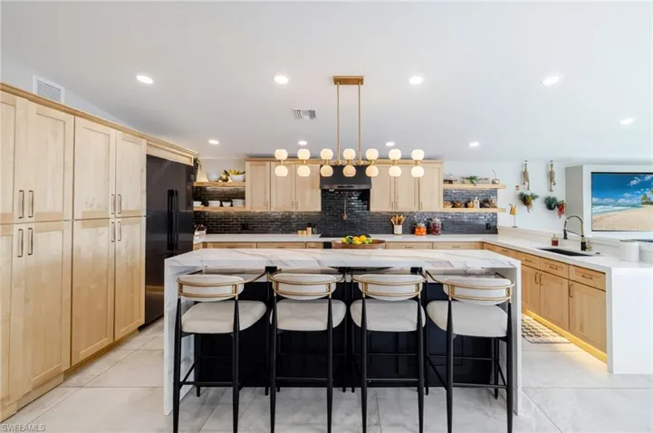 Kitchen with open shelves, a breakfast bar area, light wood finish cabinets, light stone counters, and pendant lighting