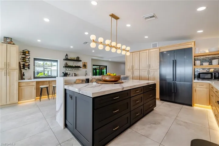 Dual tone kitchen featuring dual tone cabinetry, open shelves, vaulted ceiling, built in fridge, and a center island
