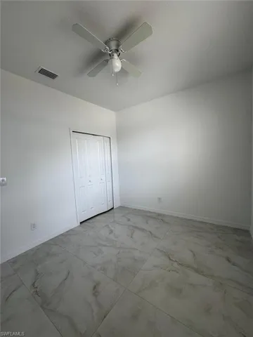 Unfurnished bedroom featuring ceiling fan, a closet, and light marble finish flooring