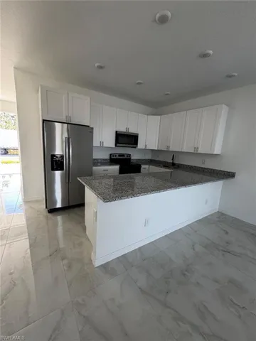 Kitchen featuring appliances with stainless steel finishes, light marble finish flooring, white cabinets, dark stone countertops, and a peninsula