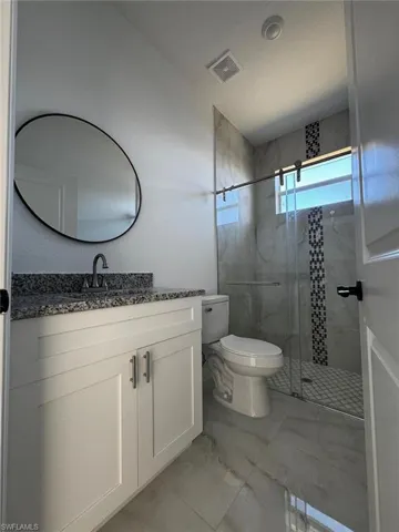 Bathroom featuring vanity, light marble finish flooring, and a marble finish shower
