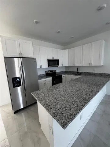 Kitchen featuring white cabinetry, dark stone counters, stainless steel appliances, and a peninsula