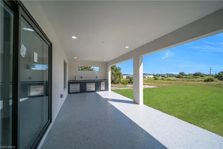 Expansive covered patio featuring an outdoor kitchen with integrated stainless-steel appliances and a sink