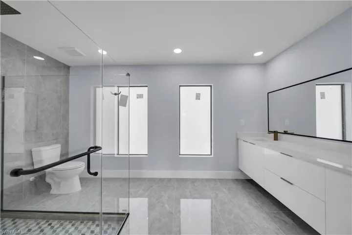 Contemporary bathroom featuring a spacious glass-enclosed shower, a floating double vanity with a white countertop, large format gray tile flooring, recessed lighting, and a wall-mounted mirror with a black frame