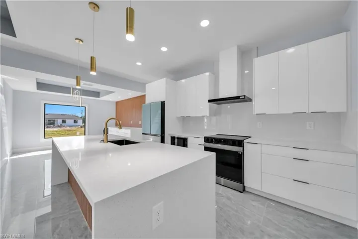 Modern kitchen showcasing a waterfall island with an undermount sink and brass faucet, white high-gloss cabinetry, stainless steel appliances, and large format gray tile flooring