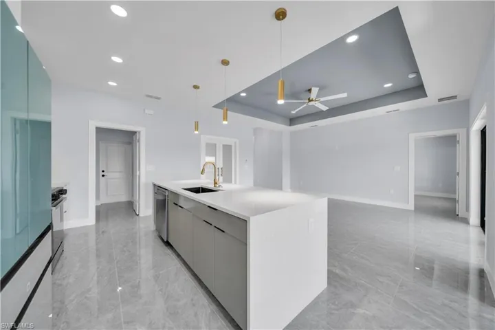 Kitchen island with a waterfall countertop and integrated sink, stainless steel appliances, recessed lighting, and large format tile flooring