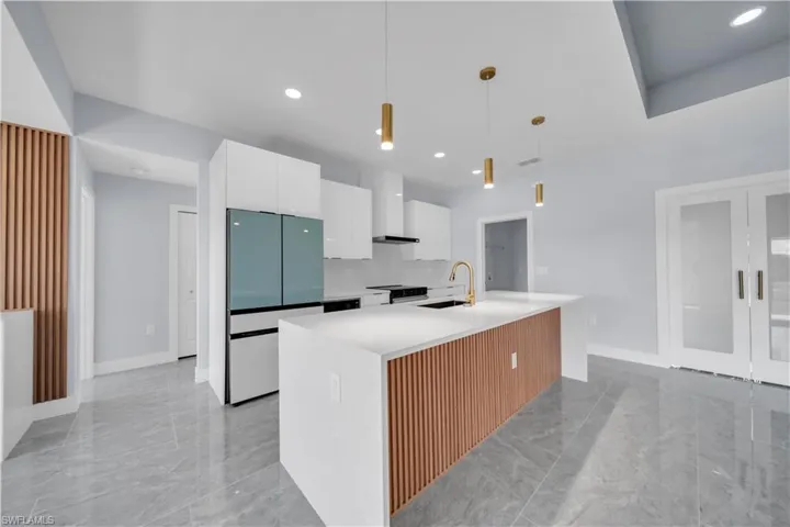 Modern kitchen featuring a large center island with a wood-slat accent panel and white countertop, complemented by sleek white cabinetry