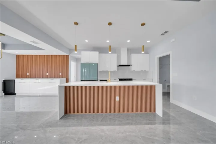 Modern kitchen featuring a large center island with slatted wood-look paneling, white countertops, and three gold-finish pendant lights