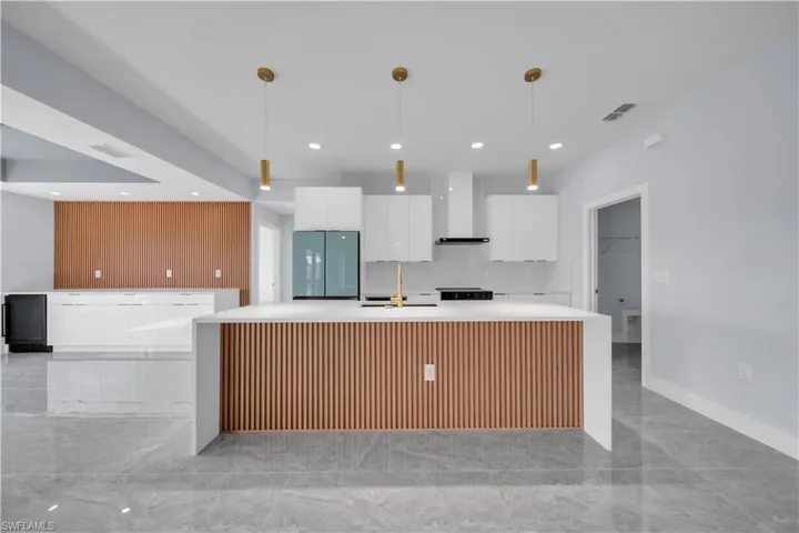 Kitchen featuring a waterfall island with wood-slat detailing, white cabinetry, integrated stainless steel appliances, pendant lighting, and large format floor tiling