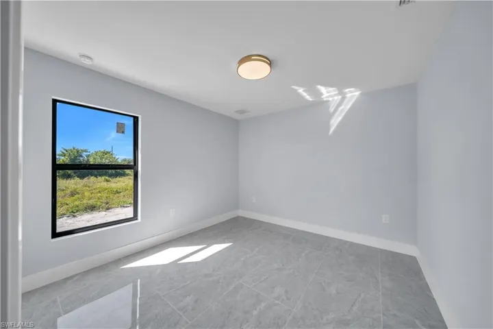 Bright room featuring a black-framed window, gray tile flooring, light gray walls, and a contemporary ceiling light fixture