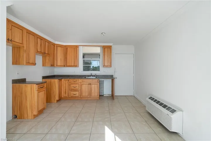 Kitchen with an AC wall unit, dark countertops, brown cabinets, light tile patterned flooring, and crown molding