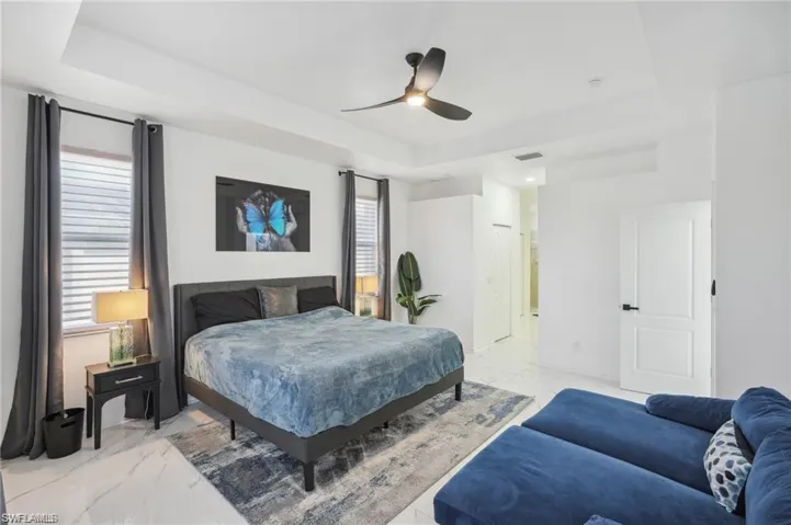 Bedroom with marble finish floor, visible vents, ceiling fan, and a tray ceiling