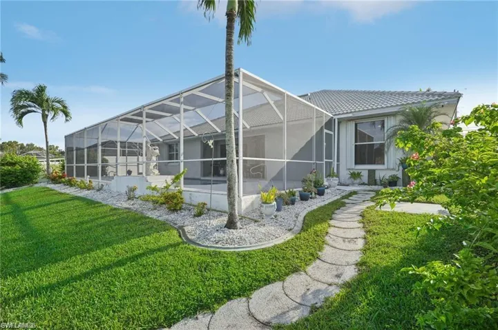 Rear view of house with a tiled roof, a patio, glass enclosure, stucco siding, and a lawn