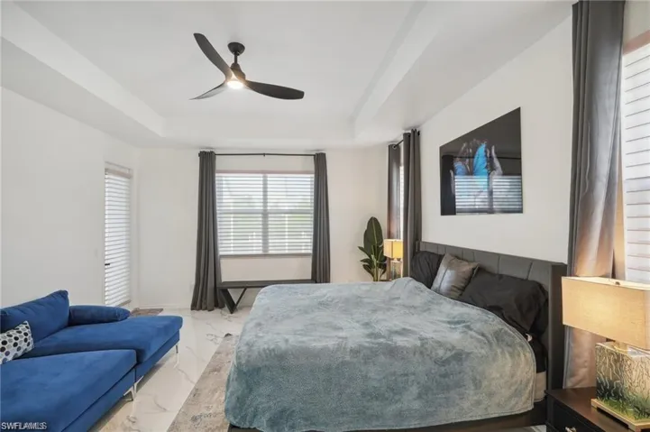 Bedroom featuring a tray ceiling, marble finish floor, and a ceiling fan