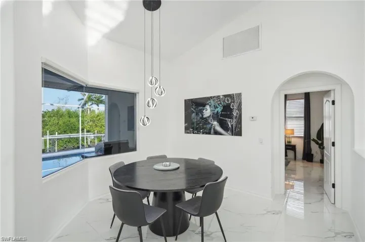 Dining area featuring high vaulted ceiling, marble finish floor, baseboards, visible vents, and arched walkways